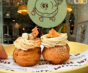 two creampuffs topped with frosting on plate in from of store window